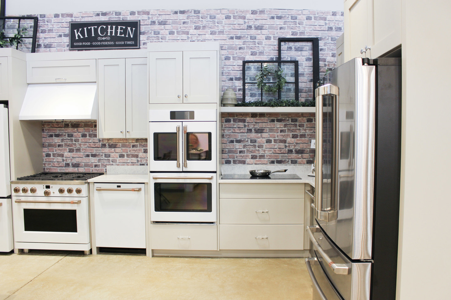 White kitchen appliance display with a range, stacked ovens and a stainless-steel refrigerator.